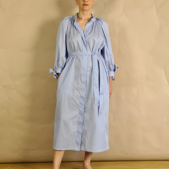 Model wearing white and blue striped cotton shirt dress with puff sleeves with belt with one hand in pocket