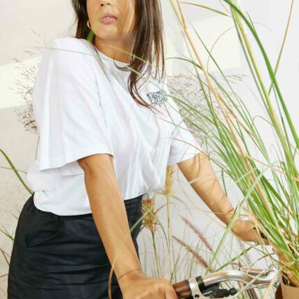 Woman wearing the Asmuss Evelyn tshirt in white with black and pink rose square hand embroidery while riding a bike with grasses in the basket