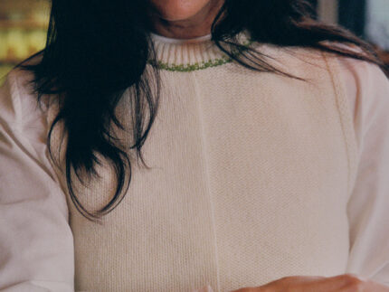 Close-up detail of cream Ada Sweater Vest showing textured half-purl, half-jersey lambswool knit and moss green contrast stitching at neckline.
