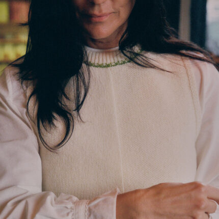 Close-up detail of cream Ada Sweater Vest showing textured half-purl, half-jersey lambswool knit and moss green contrast stitching at neckline.