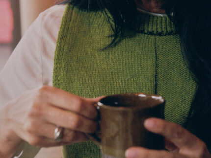 Close-up detail of moss green Ada Sweater Vest showing textured half-purl, half-jersey lambswool knit and midnight navy contrast stitching at neckline.