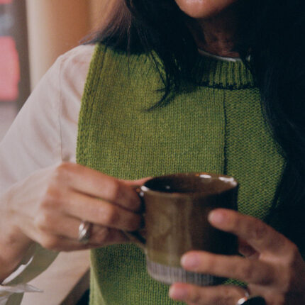 Close-up detail of moss green Ada Sweater Vest showing textured half-purl, half-jersey lambswool knit and midnight navy contrast stitching at neckline.