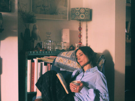 Woman in Edi pale blue shirt with Amelia navy check trousers in cosy reading scene