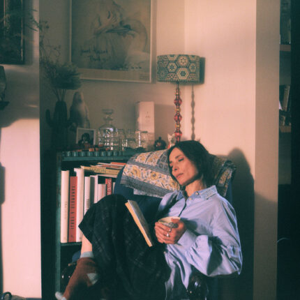 Woman in Edi pale blue shirt with Amelia navy check trousers in cosy reading scene