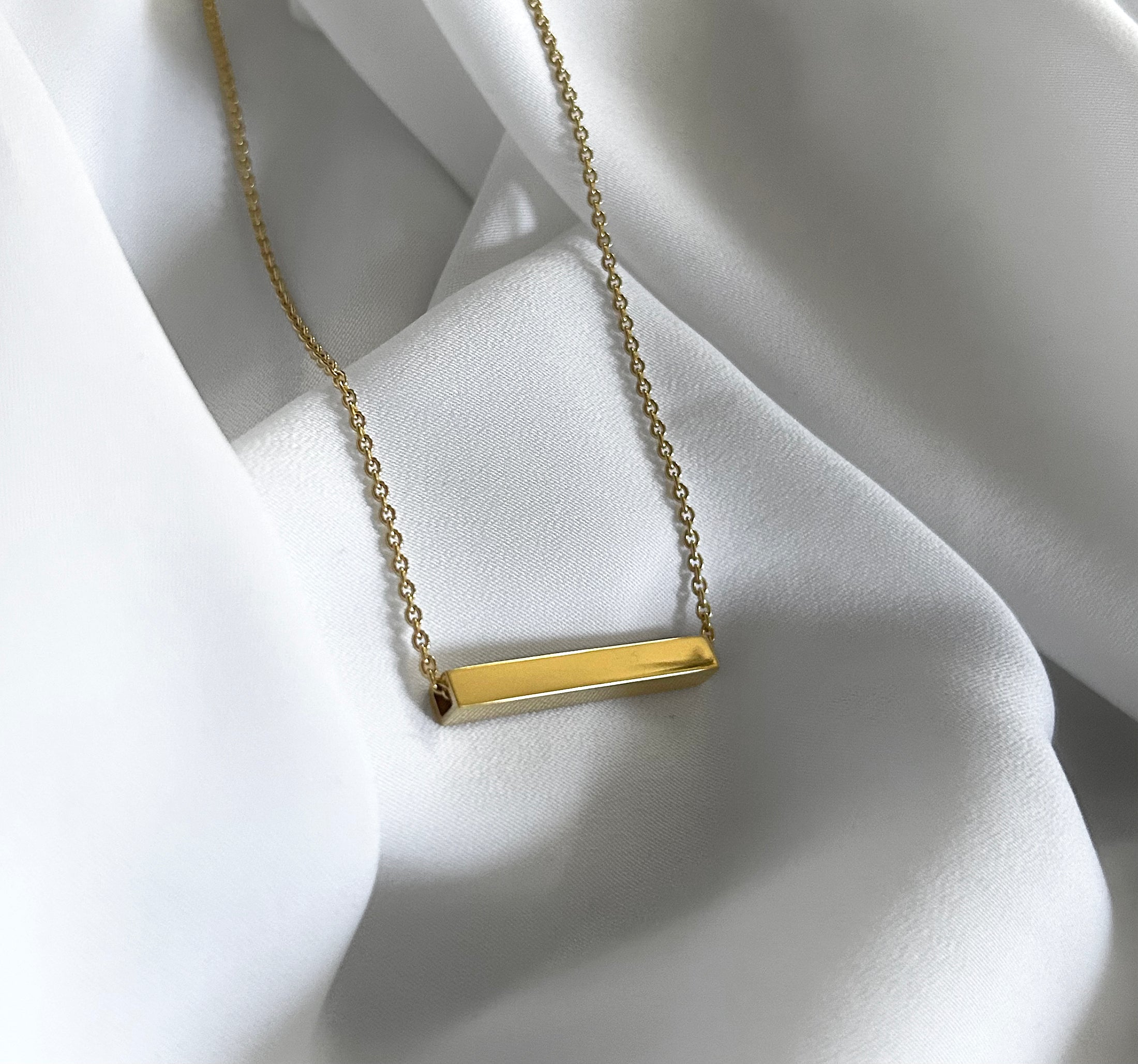 Gold necklace with a bar pendant on a white fabric background