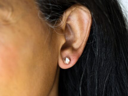 Close-up of an ear wearing a diamond-shaped earring with blurred background