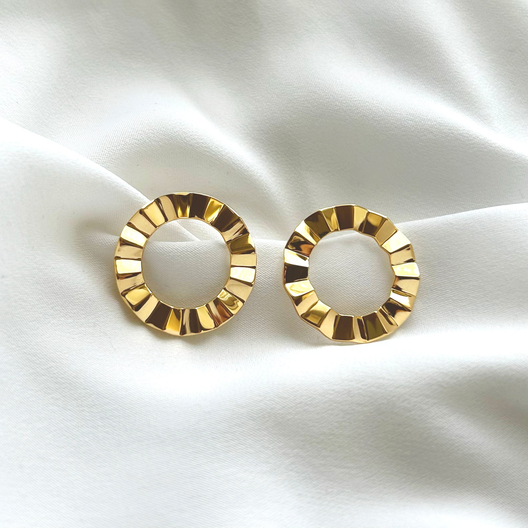 Gold circular earrings on a white fabric background