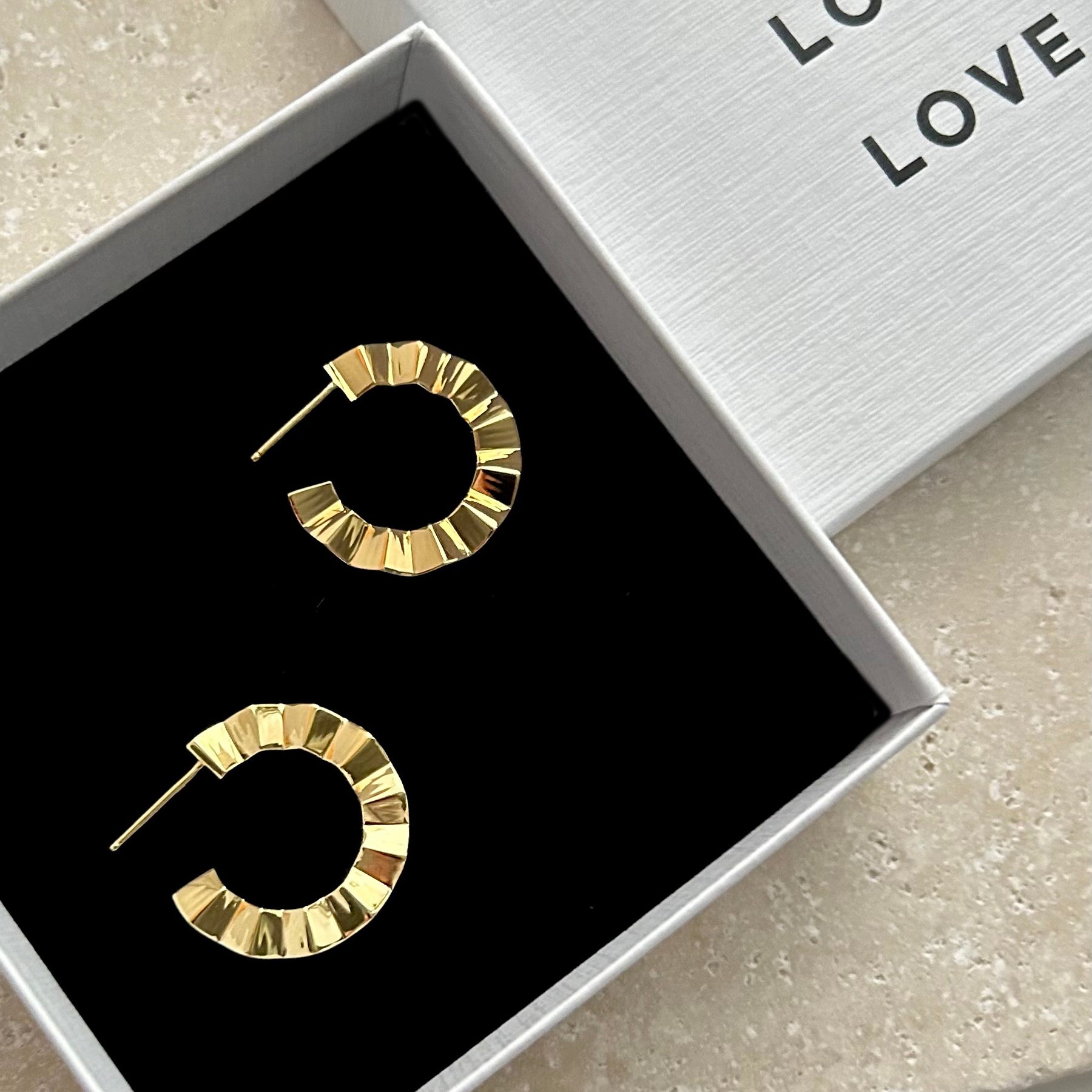 Gold hoop earrings in a box with 'LOVE' text on a light surface