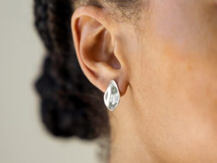 Close-up of an ear wearing a silver petal earring with blurred background