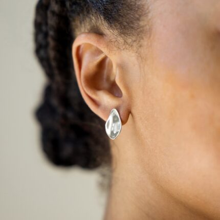 Close-up of an ear wearing a silver petal earring with blurred background