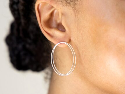 Close-up of an ear wearing a silver hoop earring with blurred hair and background