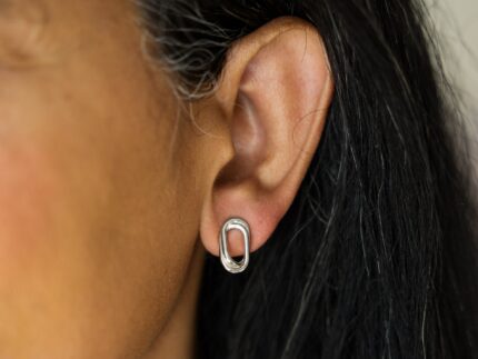 Close-up of an ear wearing a silver oval earring with dark hair.