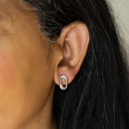 Close-up of an ear wearing a silver oval earring with dark hair.