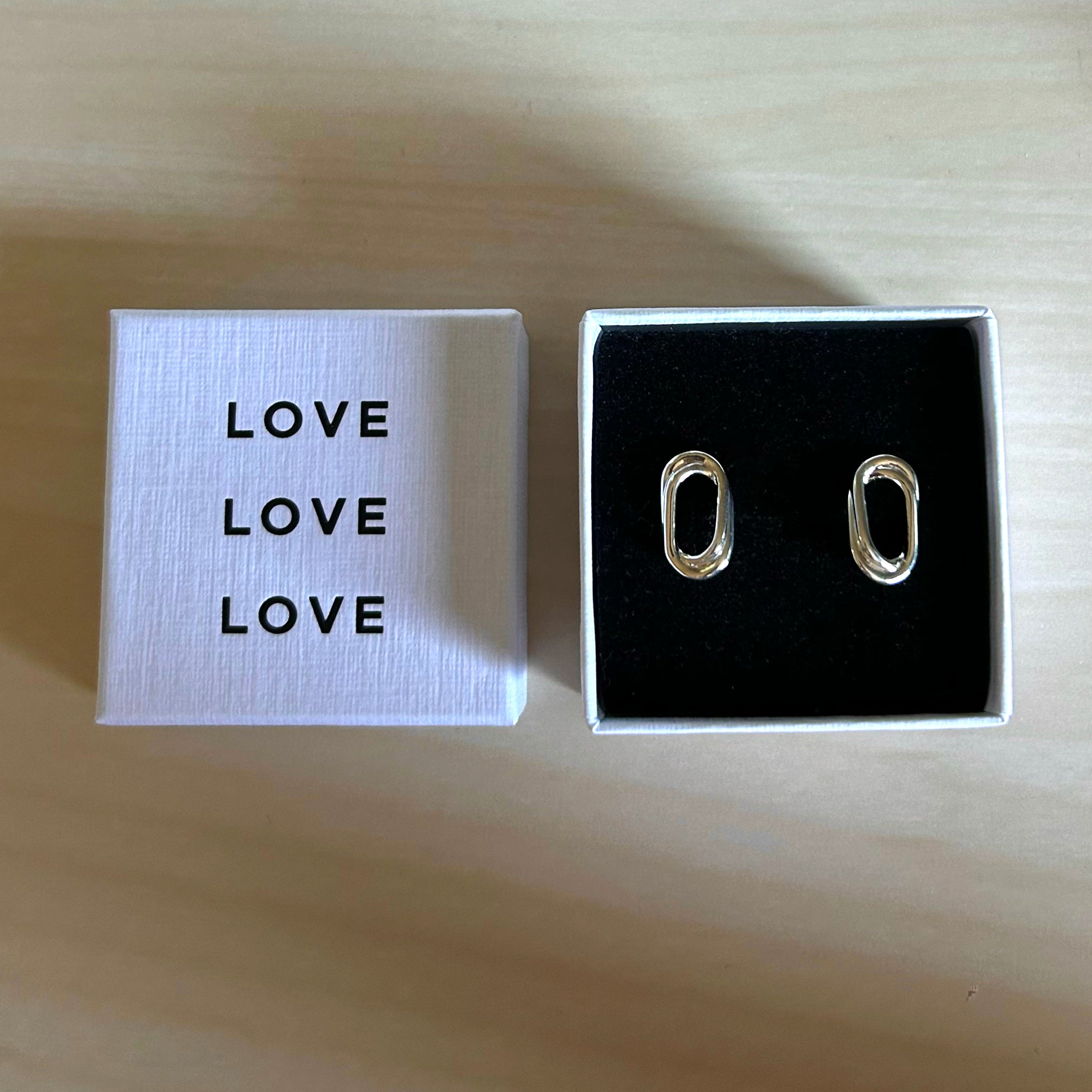Silver oval earrings in a box with 'LOVE' text on a wooden surface