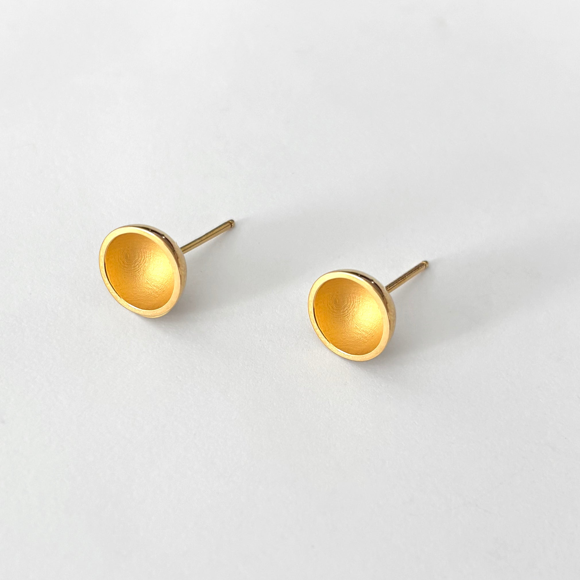 Pair of gold stud earrings on a light gray background