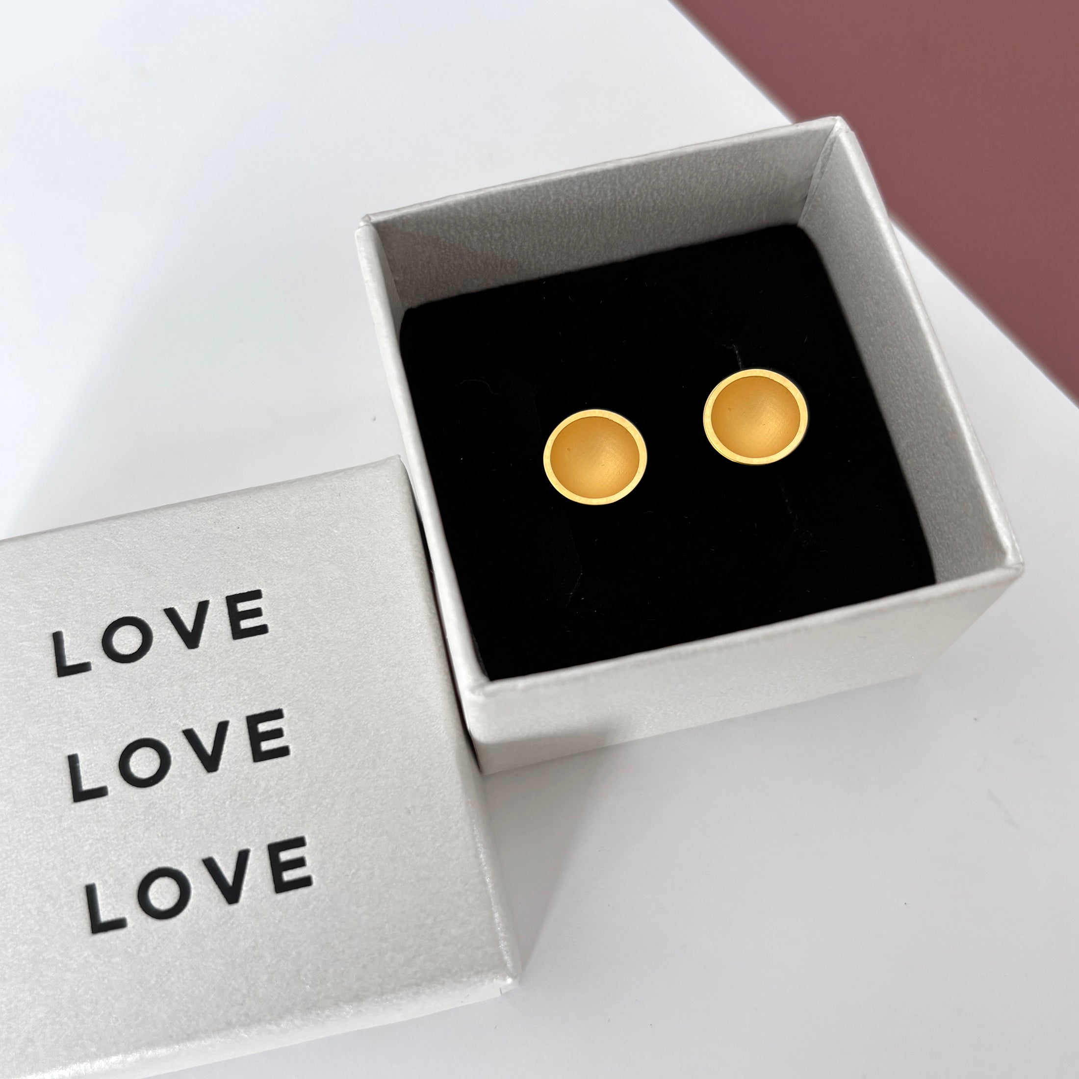 Gold earrings in a box with 'LOVE' card on a white background