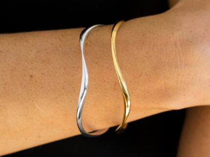 Gold and silver bangles on a wrist against a black background