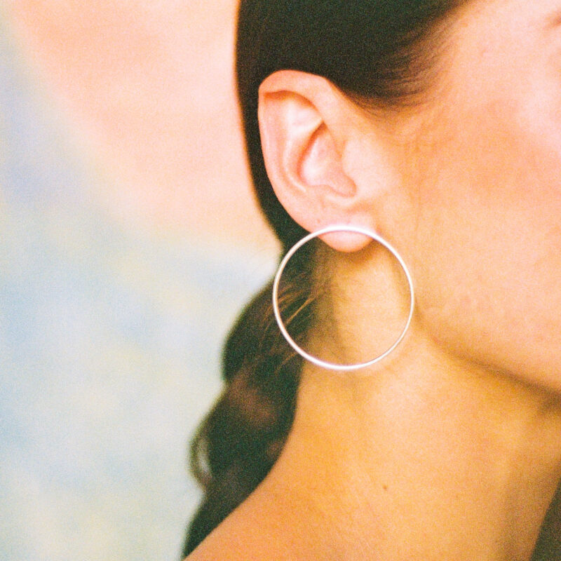 Close up of a person wearing a silver hoop earring against a blurred background
