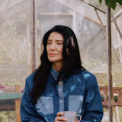 Woman with tea at greenhouse wearing Lela indigo Japanese denim patchwork shirt and Amelia trousers
