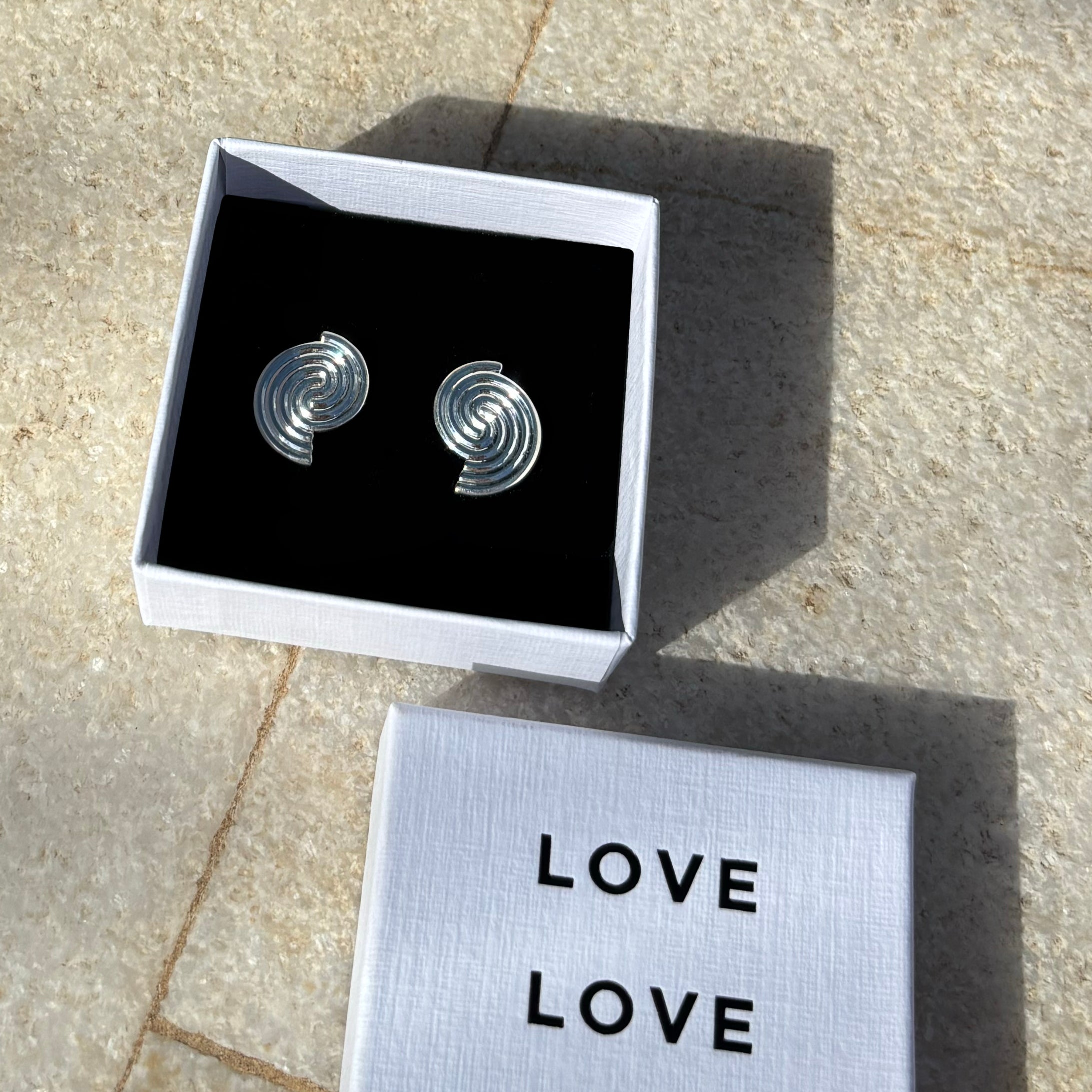 Silver spiral earrings in a box with 'LOVE' card on stone surface