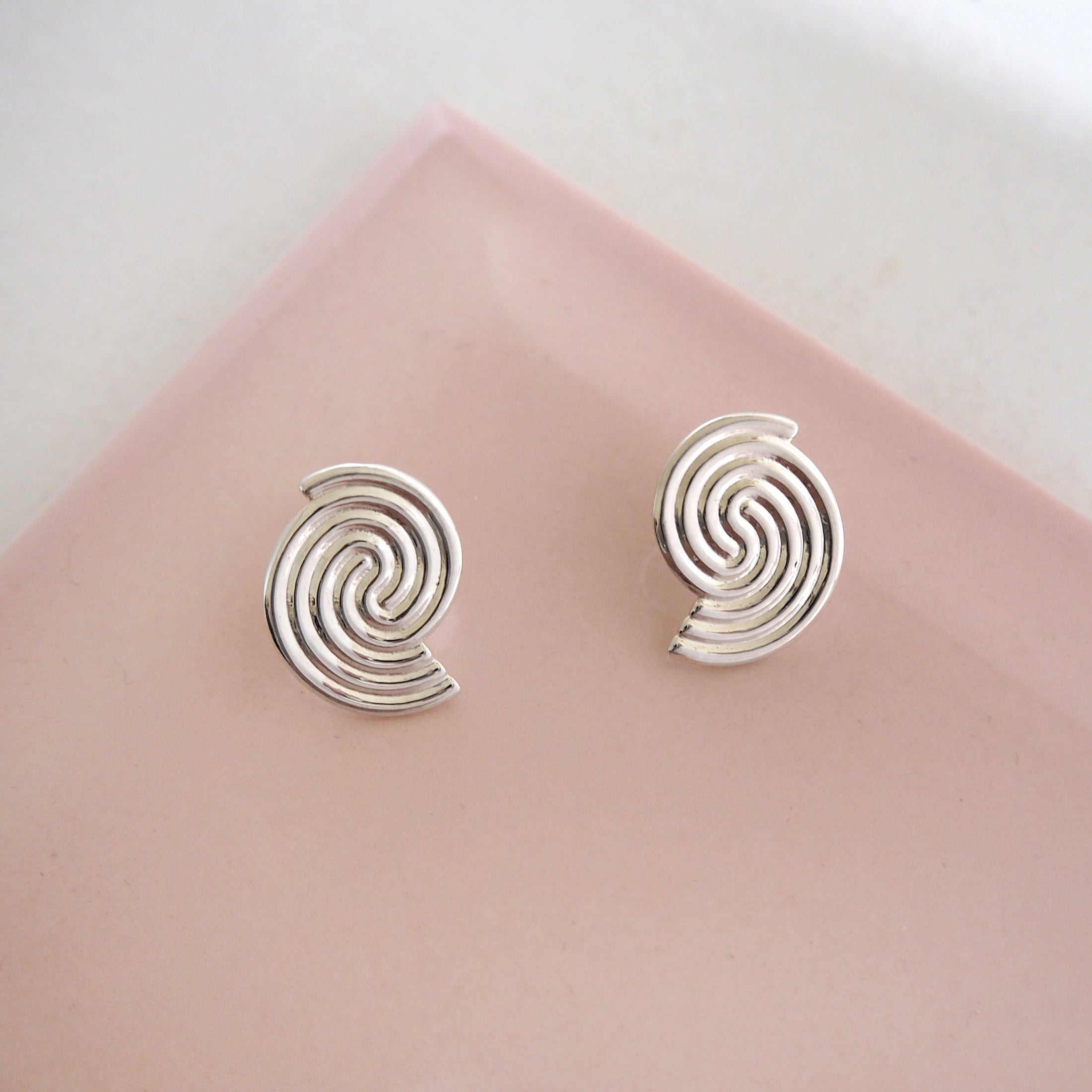Silver spiral earrings on a pink fabric background