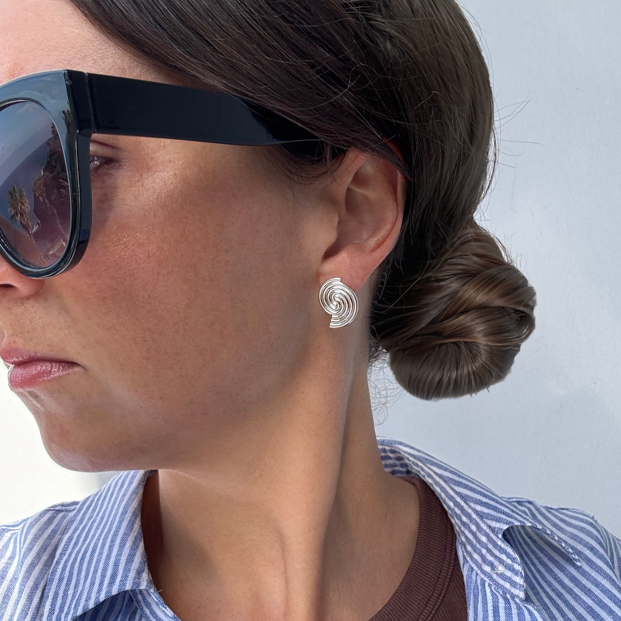 Woman wearing sunglasses and a swirl earring against a light background