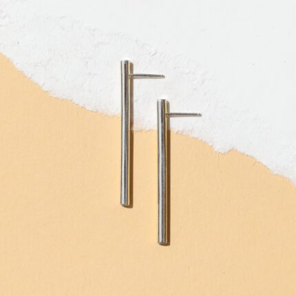 A pair of silver-colored linear drop line earrings with a tubular design, displayed against a white background.