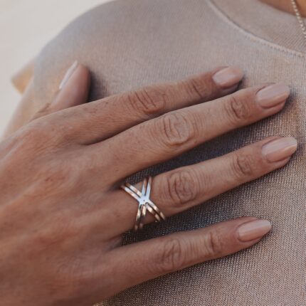 Close up of a hand wearing a geometric statement ring with a double X design.