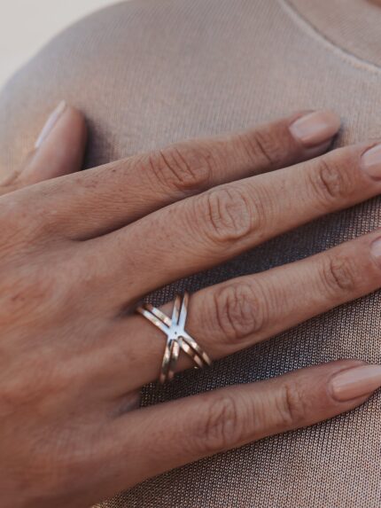 Close up of a hand wearing a geometric statement ring with a double X design.